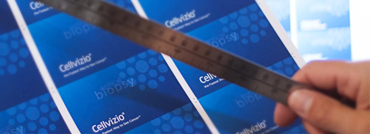 A fan of blue printed sell sheets being squared up by hand under a steel rule on the shop worktop
