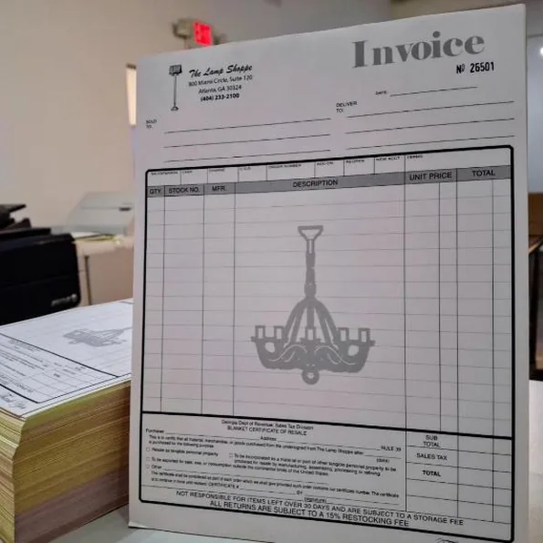A multi-part NCR invoice book with a chandelier watermark, numbered 26501, beside a padded stack of the same forms