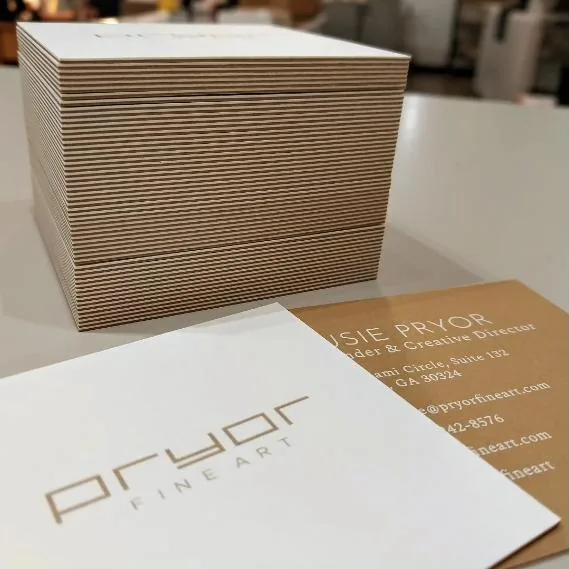 A thick stack of duplexed cards showing striped kraft core layers along the edge, beside a copper-foil business card