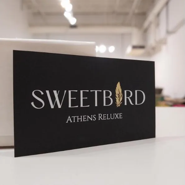 A black business card with a gold-foil feather standing in for a letter, propped on the shop worktop
