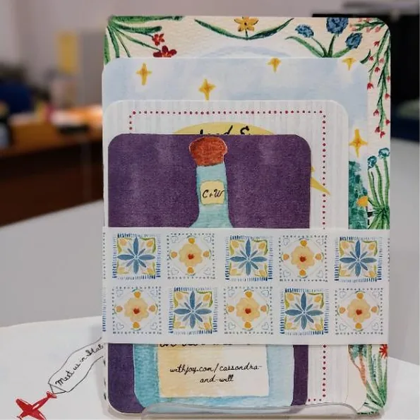 A hand-painted watercolour wedding invitation suite with layered cards and a patterned belly band of stamp motifs